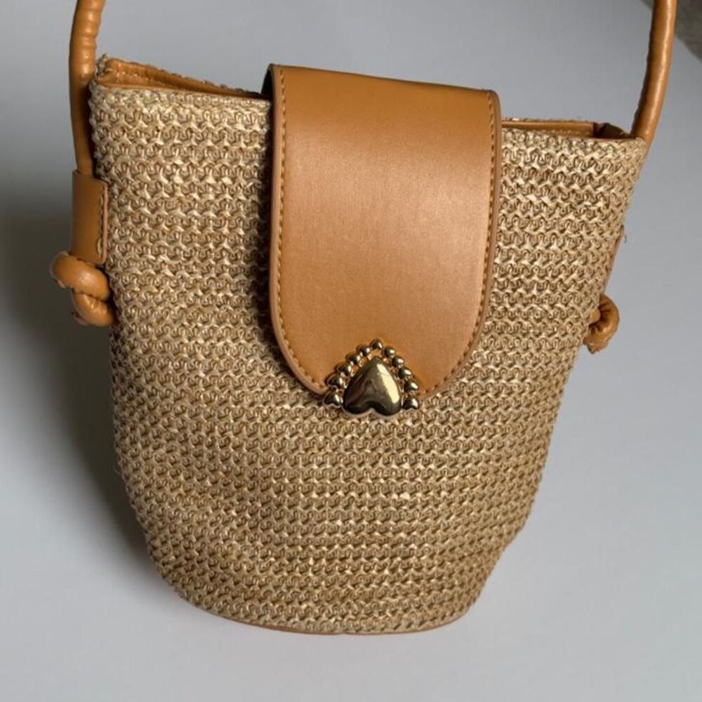 Tan woven straw bucket bag with leather accents and zipper closure